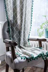 Detail of green geometric pattern curtain fabric with decorative tassels on an armchair