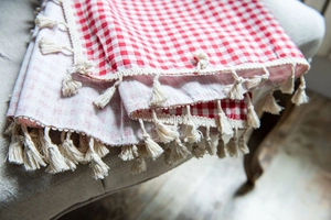 Close-up of red and white gingham fabric texture with decorative cream cotton fringe