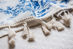 Close-up of blue Toile de Jouy print on cotton linen fabric with elegant cream tassels