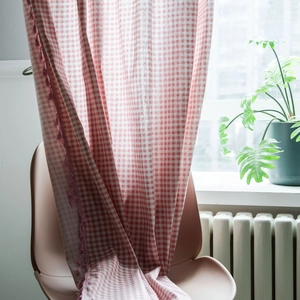 Pink and white gingham curtain with fringe trim in a bright home interior setting