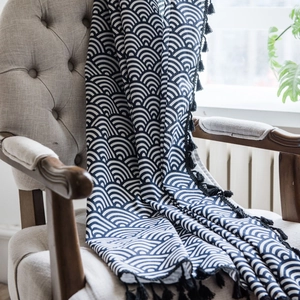 Japanese Seigaiha wave pattern navy throw blanket with tassels on a gray armchair
