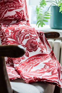 Detail of red Baroque floral printed cotton linen curtain draped over a wooden rocker