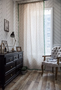 Detail of green floral curtain with pom-pom fringe against a cozy vintage home interior