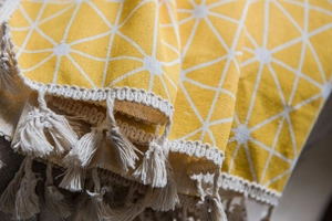 Macro detail of yellow geometric fabric with white star pattern and gray tassel fringe