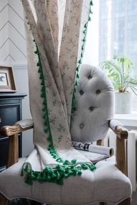 Floral print curtain with green tassel trim draped over a grey armchair in a cozy room