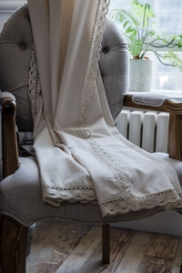 Close-up of beige cotton linen fabric with elegant crochet lace edge on a grey armchair