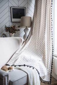 Detail of linen daisy print curtain with black tassels in a cozy home setting