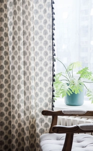 Detail of linen curtains with black tree prints and tassel trim in a sunny kitchen setting