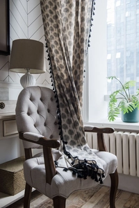 Detail of cotton linen curtain with tree print and black tassel fringe on an armchair