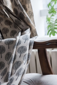 Detail of cotton linen cafe curtain with black tree prints draped on a wooden chair