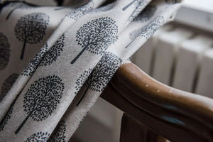 Close-up of rustic cotton linen fabric with black tree print and fringe details on wood