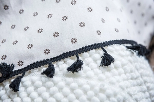 Detail of floral linen fabric with black tassel trim and white 3D pom-pom texture