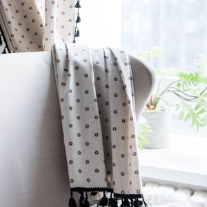 Linen cotton small daisy print curtain with black tassels draped over a sofa chair