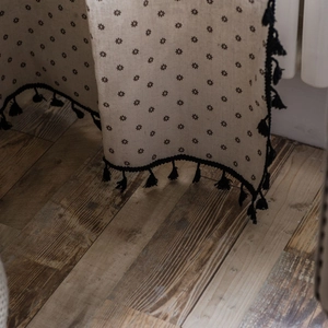Linen cotton daisy print curtain with black fringe trim on a vintage wood floor