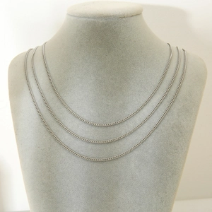 Close-up of three silver stainless steel curb chains layered on a grey neck display stand