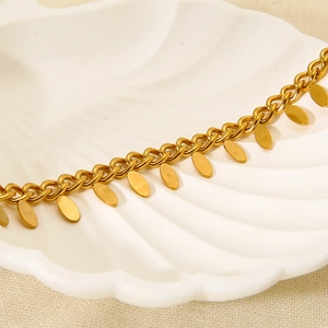 Dettaglio del bracciale dorato in acciaio inossidabile con pendenti su vassoio bianco