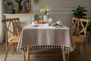 Detailed view of beige jacquard tablecloth with wave texture and white fringe tassels