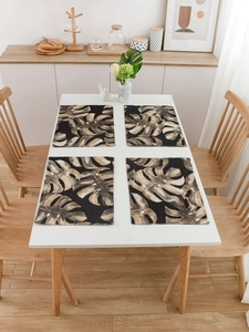 Detail view of tropical monstera leaf placemats in black and brown on a white dining table