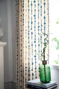 Détail du motif vagues verticales bleues sur rideaux beiges avec pompons décoratifs