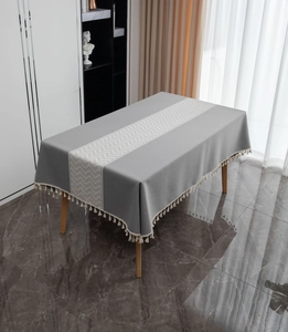 Detail of grey geometric jacquard tablecloth featuring cream fringe tassels and linen texture