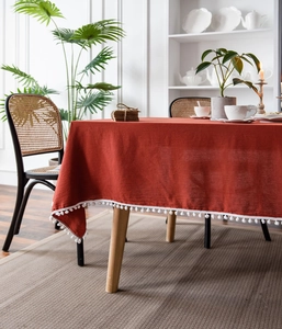 Detailansicht der orangen Leinentischdecke mit dekorativen weißen Pompons an der Kante