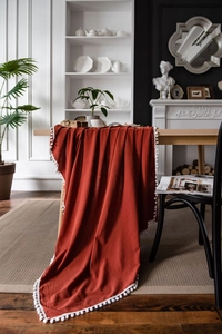 Detailansicht der ziegelroten Tischdecke mit weißen Pompons auf einem Holzesstisch