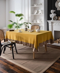 Detail of yellow cotton tablecloth with khaki ruffled edges on a wooden dining table