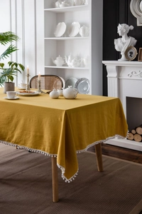 Detail of mustard yellow washed cotton tablecloth with white pom-pom lace edge decor