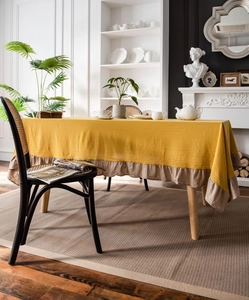 Detailed macro view showing yellow washed cotton tablecloth with beige ruffled edge trim