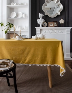Detailed texture of mustard yellow cotton tablecloth with white decorative pom pom fringe