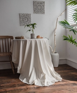 Detail of creamy white washed cotton tablecloth with elegant ruffled hem for round tables