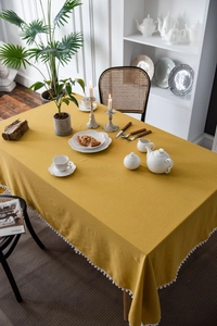 Detailed close-up of mustard yellow tablecloth featuring white pom-pom fringe edges