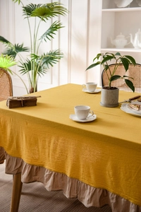 Detailed texture of yellow linen tablecloth with ruffled brown decorative hem in home setting