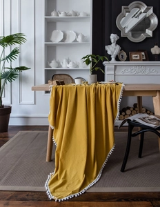 Detail of yellow washed cotton tablecloth with white pom-pom trim and fabric texture