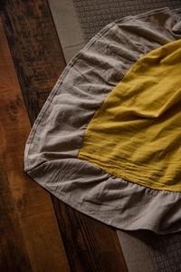 Detailed view of yellow cotton linen tablecloth with ruffled edges on wooden floor