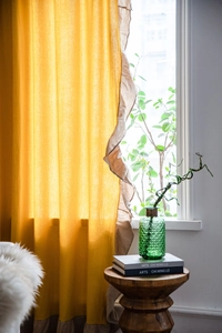 Dettaglio della tenda in lino giallo con bordi a balze beige in stanza luminosa