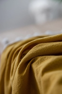 Macro shot of mustard yellow cotton tablecloth with decorative white pompom fringe detail