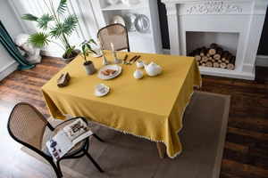Close-up of mustard yellow washed cotton tablecloth with white pom-pom fringe details