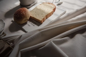 Close-up of white ruffled cotton tablecloth featuring sliced toast and sesame bread