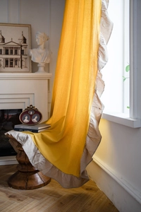 Dettaglio della tenda in lino giallo con bordo a balze e trama elegante in luce soffusa