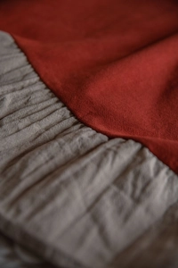 Dettaglio della cucitura a contrasto tra tessuto rosso scuro e tenda da cucina a pieghe grigio