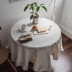 Minimalist cream white round tablecloth with elegant ruffled edges in a cozy home setting