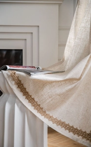 Détail du rideau en lin beige avec broderie florale foncée et bordure en corde de chanvre