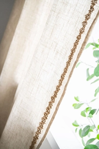 Gros plan sur la texture du rideau en lin beige avec bordure brodée marron