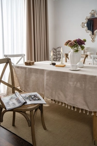 Detail shot of light beige linen tablecloth with delicate tassel edges in rustic style