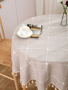 Detail of grey cotton linen round tablecloth with white lattice embroidery and elegant tassels