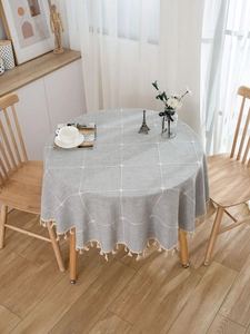 Detail of grey checkered round tablecloth with beige fringe tassels in a cozy home setting