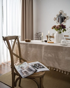 Close-up of beige linen tablecloth with decorative white fringe in a cozy dining room