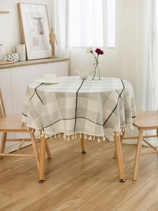 Detail of round gray plaid tablecloth with elegant cream fringe tassels on wooden table
