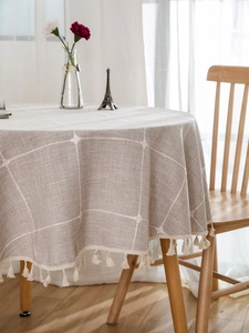 Detail of round linen-textured tablecloth with white grid pattern and beige tassels